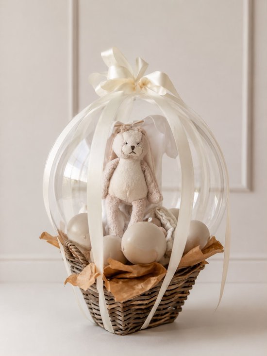 Babycadeau in ballonvorm: mandje met crèmekleurige konijnenknuffel, witte romper en decoratieve ballen.