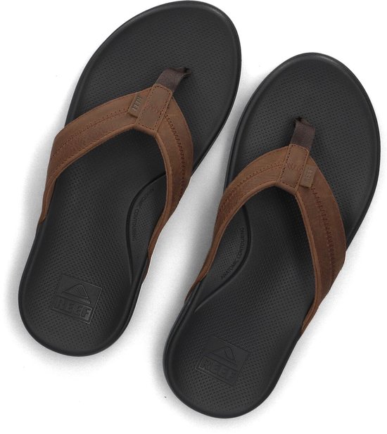 Paar bruine Reef slippers, van bovenaf gezien, met zwarte voetbedden en bruine banden.