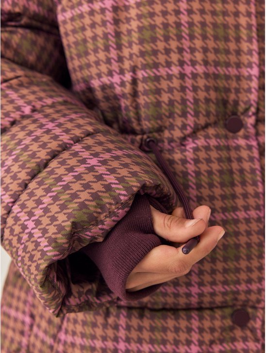 Hand van meisje in mouw van bruine jas met roze en groene ruit.