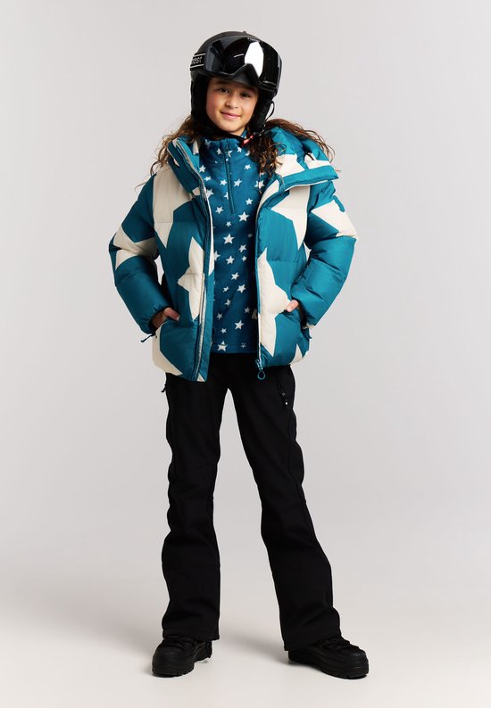 Meisje in blauwe winterjas met sterrenprint, onderlaag met sterren, zwarte skibroek en skihelm.