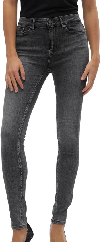 Model draagt een grijze skinny jeans met middelhoge taille en zwarte puntige pumps.