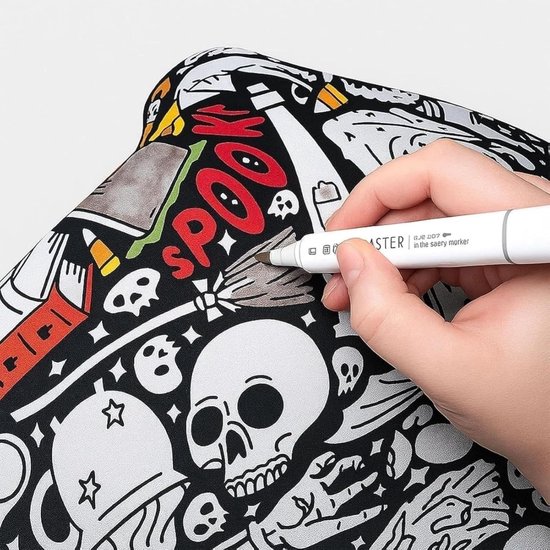 Hand kleurt met een bruine stift op een zwart-witte deken met Halloween-thema, met een spook en skelet.