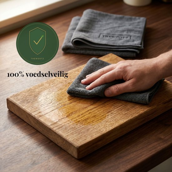 Hand die houten plank met grijze doek droogt. "100% voedselveilig" is zichtbaar.
