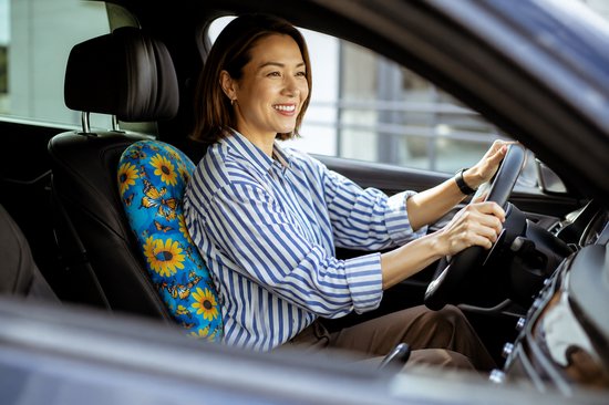 Vrouw in gestreepte blouse rijdt auto met blauw, bloemenkussen op stoel.