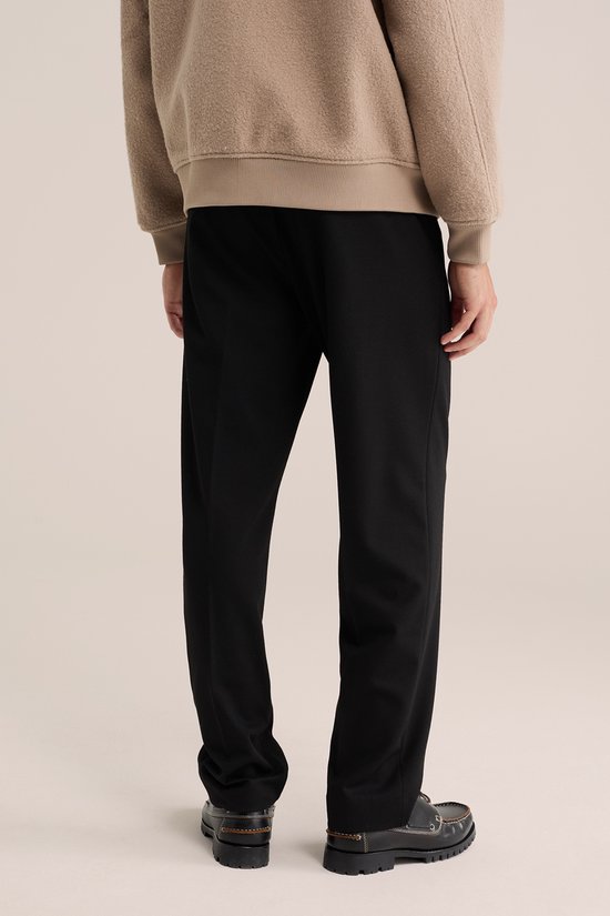 Man van achteren gezien met zwarte pantalon en beige trui.