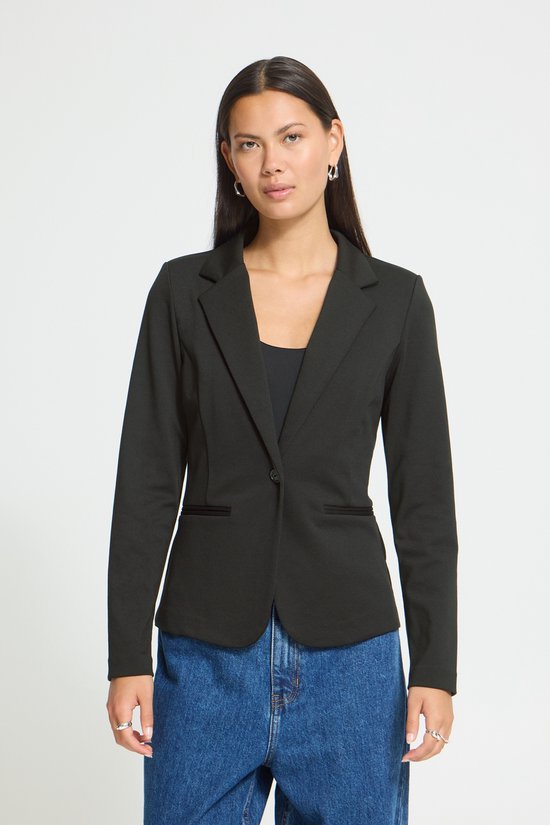 Model met lange zwarte blazer, één knoop sluiting, gedragen met een zwarte top en jeans.