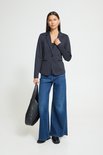 Model met donkerblauwe blazer, jeans en grote zwarte tas.