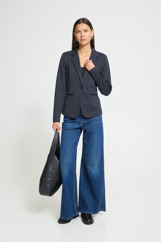 Model met donkerblauwe blazer, jeans en grote zwarte tas.