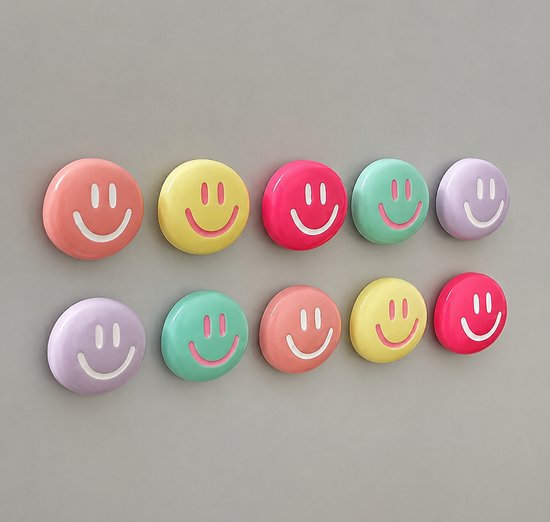 Tien ronde, 3D-smiley-magneten in pastelkleuren: roze, geel, felroze, mintgroen en paars, met witte gezichtjes op een grijze achtergrond.
