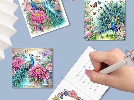 Diamond painting kaarten met pauwen, bloemen en vlinders. Een hand schrijft op een wenskaart.
