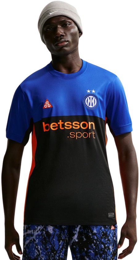 Model draagt een blauw, zwart en oranje Nike Inter Milan sportshirt met 'betsson .sport' logo op de borst. Granietkleurige muts.