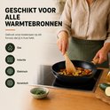 Een vrouw kookt groenten in een zwarte koekenpan met houten handvat op een inductiekookplaat.