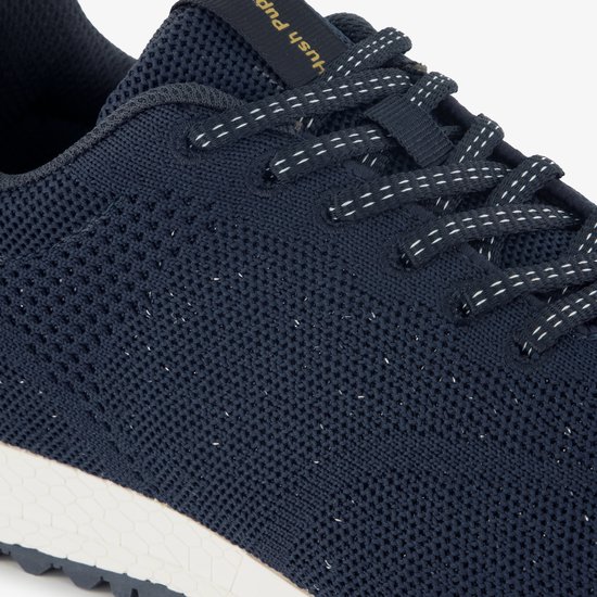 Detail van een donkerblauwe sneaker met gebreid bovenwerk en witte spikkels.