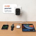 Zwarte reisadapter in stopcontact met 4 USB-poorten aangesloten op smartphone, smartwatch, oordopjes en tablet.