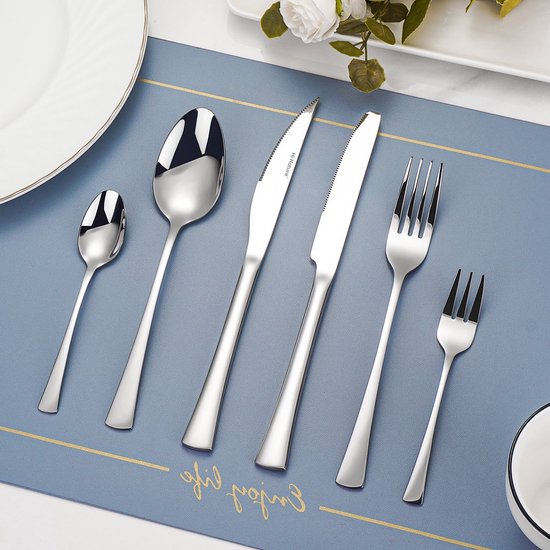 Moderne zilverkleurige bestekset op een blauwe placemat met gouden details, op een witte schaal.