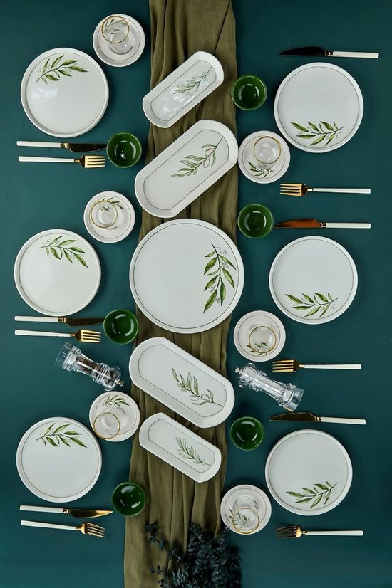 Wit servies met groene olijftakken, omringd door groene kommetjes en gouden bestek.