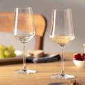 Deux élégants verres à vin blanc cristallins avec une tige fine et un calice large, légèrement conique. Un verre contient un vin jaune doré.