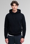 Model met donkerblauwe hoodie, kangoeroezak, witte onderlaag en donkere joggingbroek.
