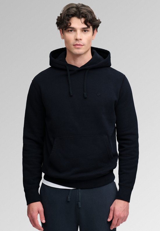Model met donkerblauwe hoodie, kangoeroezak, witte onderlaag en donkere joggingbroek.
