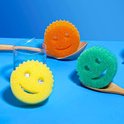 Gele, oranje en groene Scrub Daddy sponzen in een glazen potje en lepels.