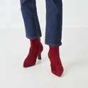 Model draagt rode suède enkellaarsjes met puntige neus, stilettohak en spijkerbroek.