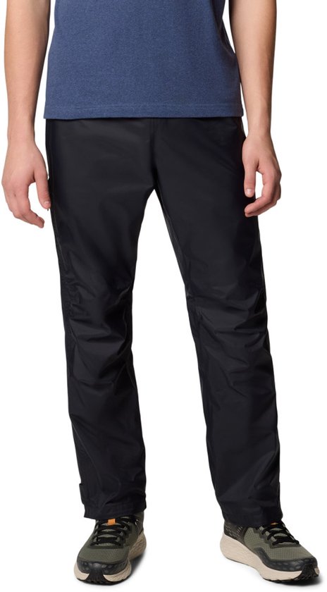 Homme portant un t-shirt bleu et un pantalon d'extérieur noir, debout sur des baskets vertes.