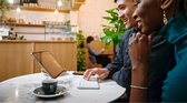 Man en vrouw kijken lachwekkend naar een tablet met toetsenbord in een café.