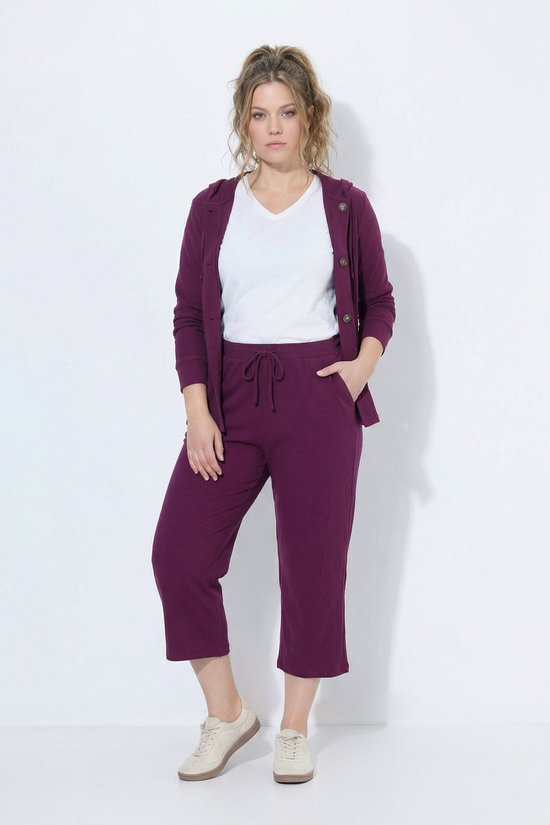 Model draagt een donkerrode sweatculotte met wafelstructuur en wijde pijpen.