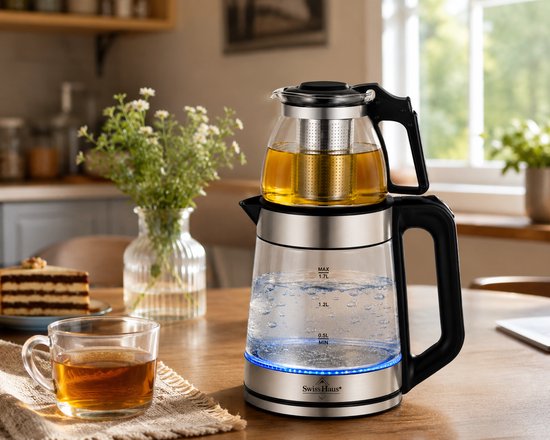 Glazen waterkoker met theepot bovenop, gevuld met thee, op een houten tafel.