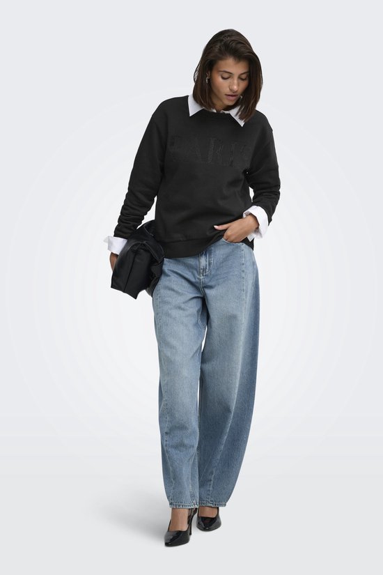 Model in zwarte sweater met parel "PARIS" opdruk, wit overhemd, jeans en zwarte tas.
