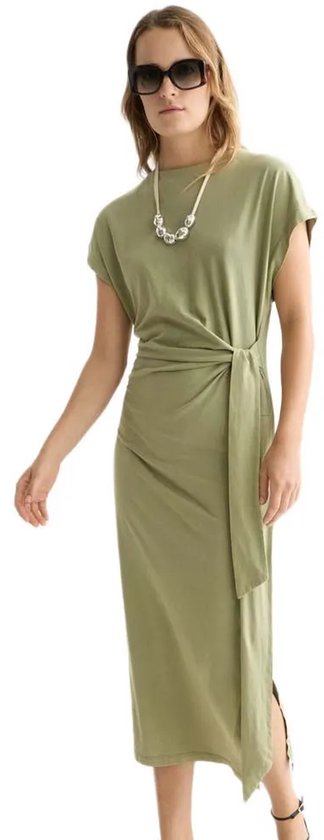 Model in olijfgroene midi-jurk met korte mouwen, strikceintuur en split aan de zijkant.