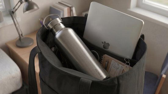 Zilverkleurige RVS thermosfles met "STAALTJE" logo in een donkergrijze tas, naast een laptop.