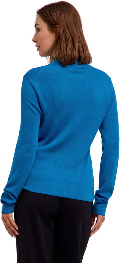 Achteraanzicht van het model in een blauwe coltrui met lange mouwen en een zwarte broek.