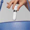 Hand met beige nagels houdt een witte Braun gezichtshaar trimmer boven een blauwe tas.