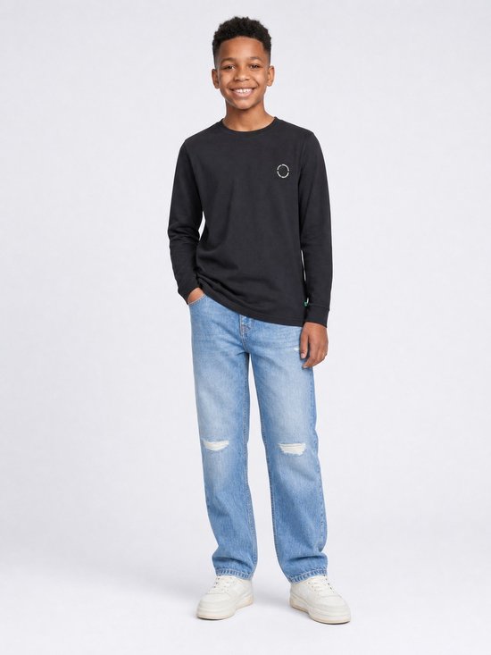 Jongen met een zwarte longsleeve en distressed jeans.