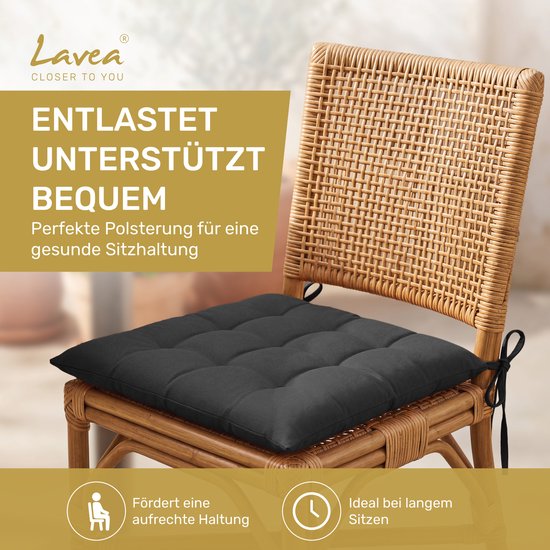 Donkergrijs zitkussen met touwtjes op een rotan stoel.