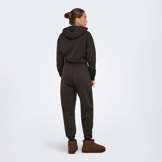 Model in een donkerbruine joggingbroek met trekkoord en capuchontrui.