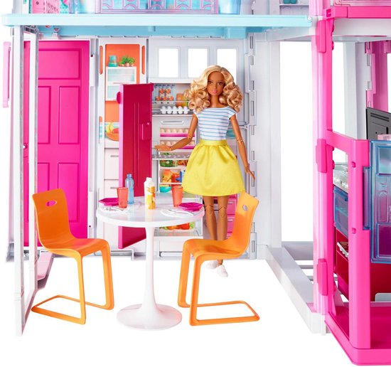 Barbie met gele rok en blauw-wit gestreept shirt in een keuken van een Barbiehuis, naast een tafel met twee oranje stoelen.