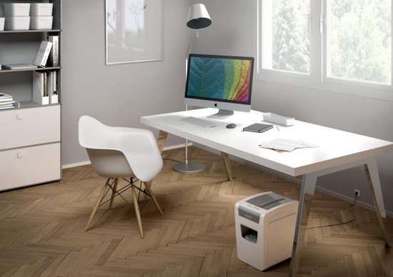 Een witte Leitz papierversnipperaar staat op de grond naast een bureau met een computer in een modern kantoor.
