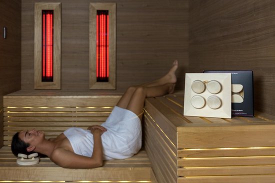Vrouw in witte handdoek ontspant in sauna op houten bankje, met een Halu hoofdkussen naast haar.