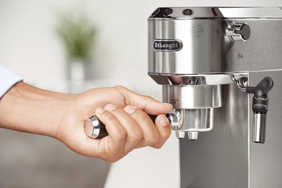 Hand draait de portafilter vast in een zilverkleurige De'Longhi espressomachine.