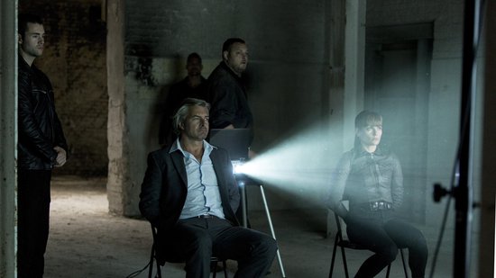 Vrouw en man zitten in donkere kamer, geprojecteerd licht op hen.