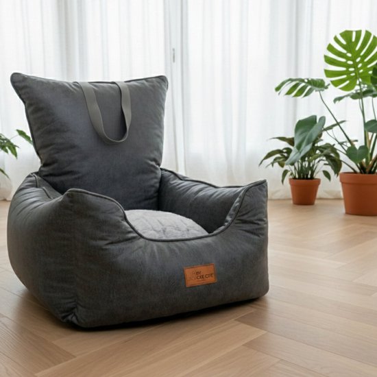 Grijze hondenmand op een houten vloer, met planten op de achtergrond.
