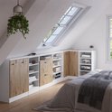 Witte opbergkasten met houten deuren en open vakken, onder een schuin dak, naast een bed.