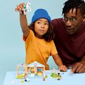 Enfant avec bonnet bleu tenant un cheval LEGO en l'air, père regardant la clinique vétérinaire LEGO.