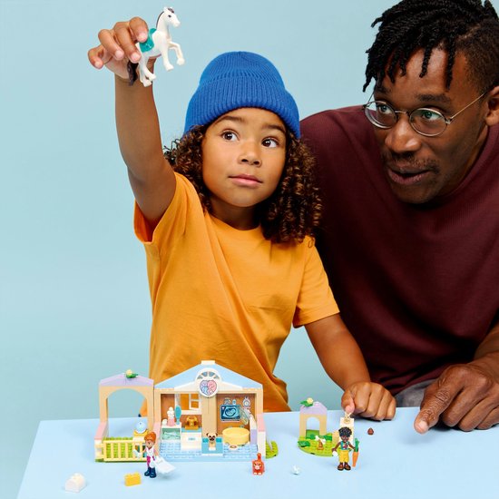 Enfant avec bonnet bleu tenant un cheval LEGO en l'air, père regardant la clinique vétérinaire LEGO.