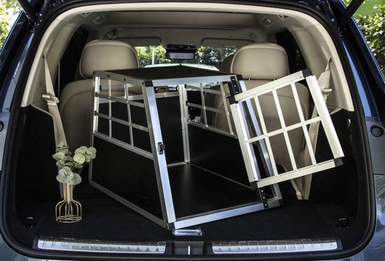 Aluminium hondenbench in de kofferbak van een auto, met een open deur.