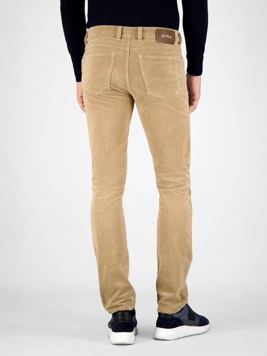 Achterkant van een man in beige corduroy broek en blauwe sneakers.