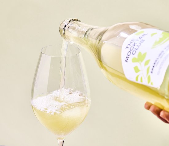Goudgele alcoholvrije Sparkling Yuzu mocktail wordt in een wijnglas geschonken vanuit een glazen fles. Met groen label.