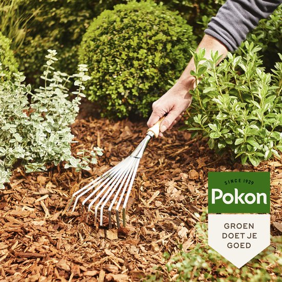 Hand met hark in boomschors tussen groene struiken. Pokon logo.